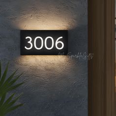 an illuminated sign on the side of a building that reads 3006, with a plant next to it