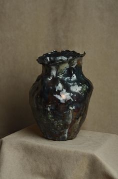 a black vase sitting on top of a table next to a brown cloth covered wall