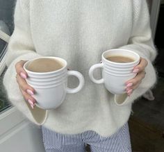 a woman holding two cups of coffee in her hands