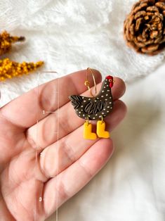 a hand holding a pair of earrings in front of a pine cone and other decorations