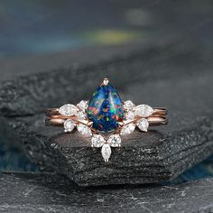 an opal and diamond ring on top of a black rock with white diamonds around it