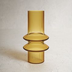 a tall yellow glass vase sitting on top of a white table next to a wall