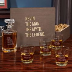 four whiskey glasses sitting on top of a wooden table next to a sign that says kevin the man, the myth the legend