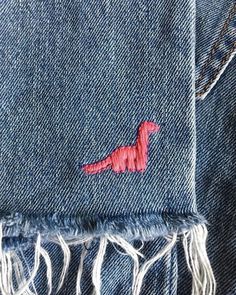 a red dinosaur embroidered on the back of a pair of blue denim jeans with fringes