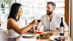 a man and woman sitting at a table with wine glasses in front of them, sharing a meal