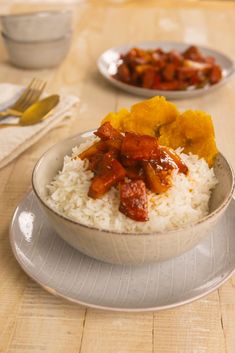 a bowl filled with rice and meat on top of a wooden table next to silverware