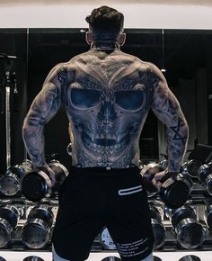 a man with tattoos on his back standing in front of some dumbbells