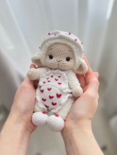 a hand holding a small crocheted doll with hearts on it's body