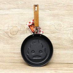 a black frying pan with a face drawn on the side and a wooden spatula