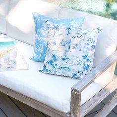 two blue and white pillows sitting on top of a wooden bench next to a pool