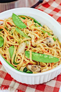 a white bowl filled with noodles and veggies on top of a checkered table cloth