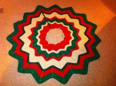 a circular crocheted rug on the floor with red, white and green colors