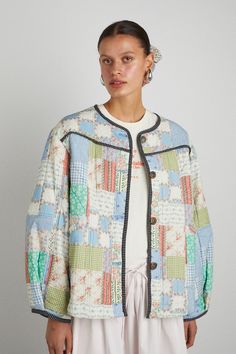 a woman standing in front of a white wall wearing a jacket with multicolored squares on it