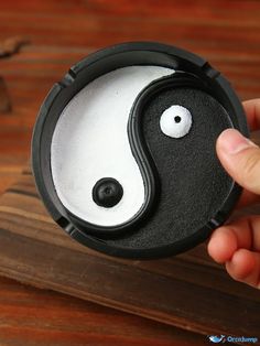 a person holding up a small black and white yin - yang box on top of a wooden table