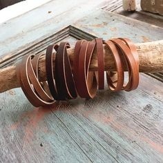 a bunch of leather bracelets sitting on top of a piece of driftwood next to a wooden stick