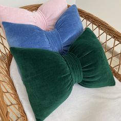 three pillows are sitting on top of a wicker chair with a white pillow behind them