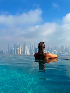 a woman sitting in the middle of a swimming pool looking out over a cityscape