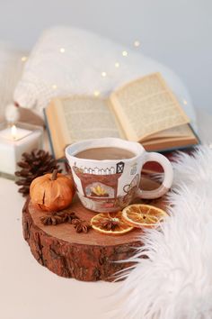 a cup of tea with orange slices and an open book on a wooden table next to a candle