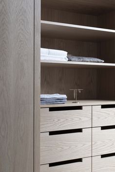 an open wooden cabinet with drawers and folded towels on the top shelf next to it