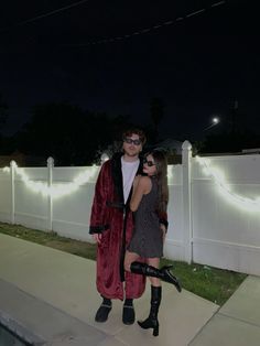 a man and woman dressed in costumes standing next to each other on a sidewalk at night