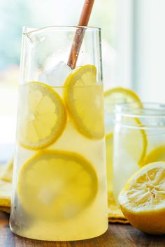 a glass filled with lemonade sitting on top of a table next to sliced lemons