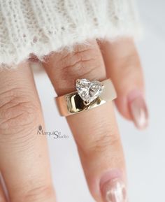 a woman's hand wearing a gold ring with a heart shaped diamond on it