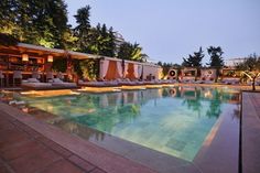 an outdoor swimming pool with lounge chairs and trees in the background at dusk or dawn