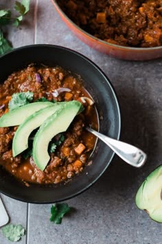 a bowl filled with chili and avocado on top of a table next to another bowl