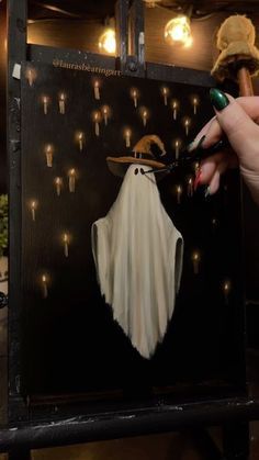 a person is painting a ghost on a black piece of wood with lights in the background