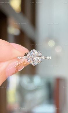 a woman's hand holding an engagement ring in front of her face, with the diamond