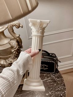 a person holding a white vase on top of a marble table next to a lamp