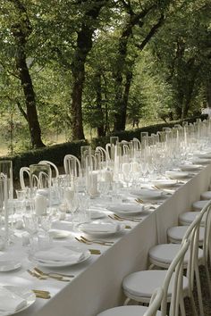 a long table is set up with white plates and silverware for an outdoor event