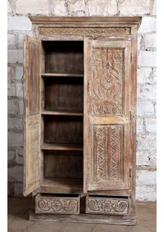 an old wooden cabinet with carvings on the doors and shelves in front of a brick wall