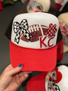 a person holding up a red and white baseball cap with the kc logo on it