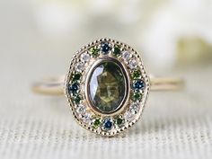 an oval shaped ring with green and blue stones on the side, sitting on a white surface