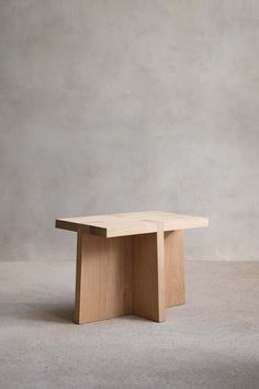 a square wooden table sitting on top of a cement floor next to a white wall