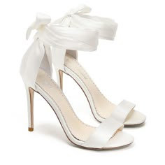 a pair of white high heeled shoes with a bow on the ankle