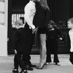 a man and woman kissing while two small children stand next to them in front of a building