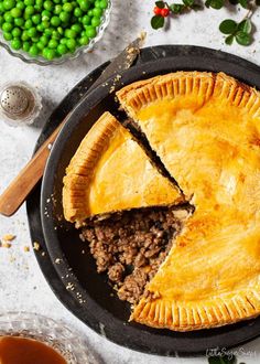 a minced beef and onion pie on a black plate with one slice cut out