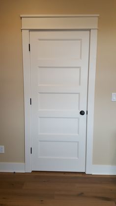 an empty room with a white door and hard wood floor