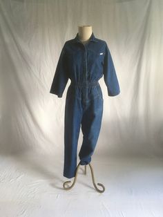 vintage 80s women's denim jumpsuit label- Dreams cotton blue jeans wide smocked elastic waist chevron chest 2 hand pockets tapered leg good vintage condition, light wear a few faded stains, light collar ring fade, knee fade (see photos) labeled size medium, see below measures, lying flat, shoulder-17" chest-18" sleeve-16" waist-13" to 15" stretched comfortably hip-19" rise-15" inseam-27" hem-6" top to waist-19" waist to hem outseam-41" total length-59"     We do not offer returns or refunds unle Vintage Non-stretch Cotton Jeans, Fitted Medium Wash Cotton Overalls, Relaxed Fit Full-length Denim Jumpsuit With Pockets, Fitted Cotton Denim Jumpsuit For Fall, Vintage Denim Jumpsuit For Work, Medium Wash Cotton Denim Jumpsuit For Fall, Fall Medium Wash Cotton Denim Jumpsuit, High Waist Medium Wash Jumpsuits For Fall, Cotton Denim Jumpsuit In Medium Wash For Fall