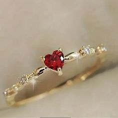 a gold ring with a heart shaped red stone and three small white stones on it