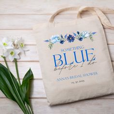 a tote bag next to some flowers on a wooden table with the words something blue before it