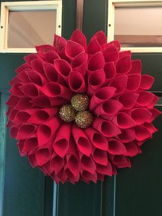 a large red flower hanging from the side of a green door with two gold balls on it