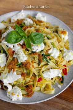 a white plate topped with pasta covered in fettuccine and basil leaves on top of a wooden table