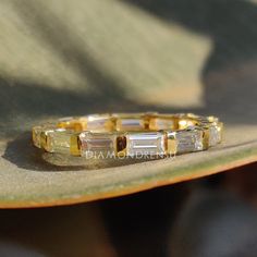 a yellow gold ring with baguettes on it sitting on top of a leaf