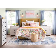 a bedroom scene with focus on the bed, dresser and nightstands that are decorated in pastel colors