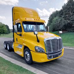 a yellow semi truck is parked on the side of the road in front of some trees