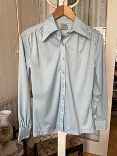 This pretty, super comfortable blouse is made of 100 per cent polyester that is stretchy, lightweight, silky and doesn't crease! It has the original buttons in the front and on the cuffs, a wide pointed collar and gathered yokes on the front and back. In very good vintage condition. Marked size 13, but vintage sizes are often much smaller than today's. The measurements, taken with the blouse lying flat, are: shoulder to shoulder, 16 inches; armpit to armpit, 19 1/2 inches; sleeves, 24 1/2 inches; overall length, 26 inches; bottom edge, 18 inches. Baby Blue Shirt, Comfortable Blouses, Vintage Sweaters, Vintage Baby, Blue Shirt, Size 13, Womens Clothing Tops, Denim Button Up, Baby Blue