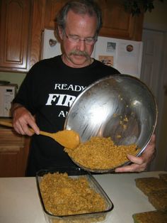 a man holding a metal pan filled with food on top of a counter next to a wooden spoon